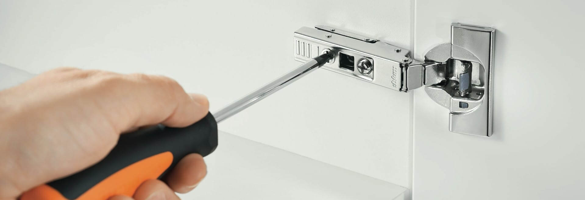 person with a screwdriver adjusting a cabinet hinge